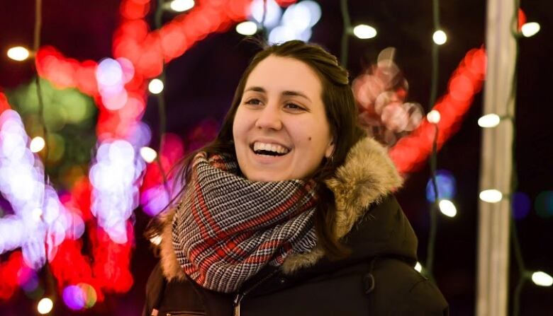 A woman smiles in front of hanging Christmas lights.