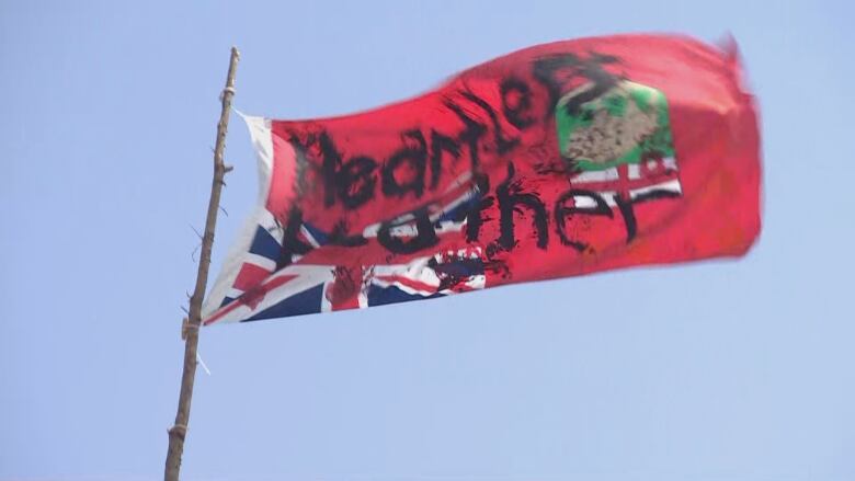 A red Manitoba provincial flag blows in the wind with the words Heartless Heather written on it.