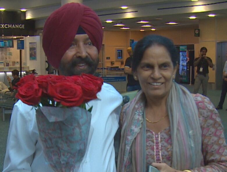 A man and a woman put their arms around each other at YVR airport. The man is holding roses.