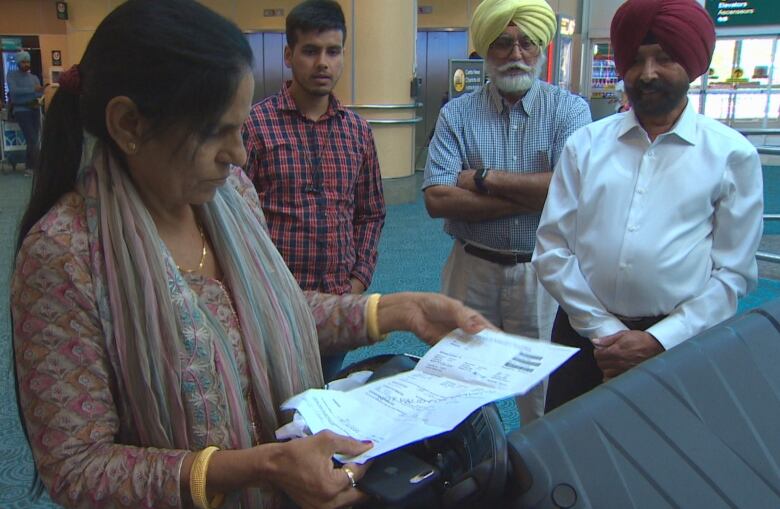 A woman looks over paperwork while a young man and two older men look toward her.