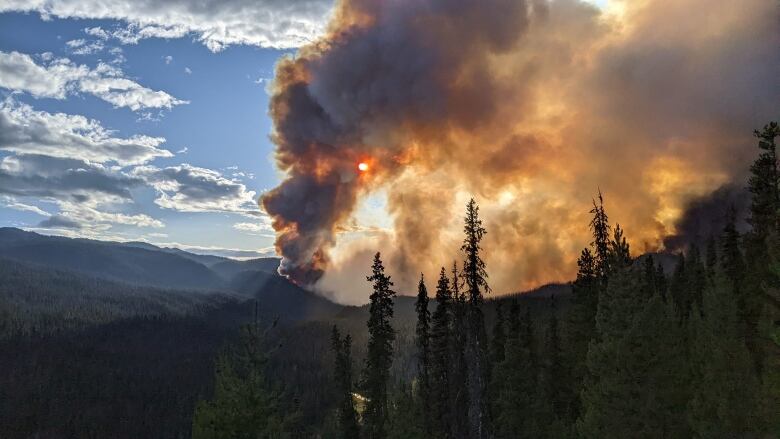 Plumes of grey smoke are seen during sunset, giving the wildfire smoke an orange hue.