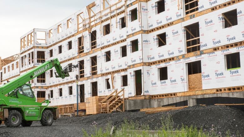 A green crane lift is pictured in front of an under construction apartment building. 