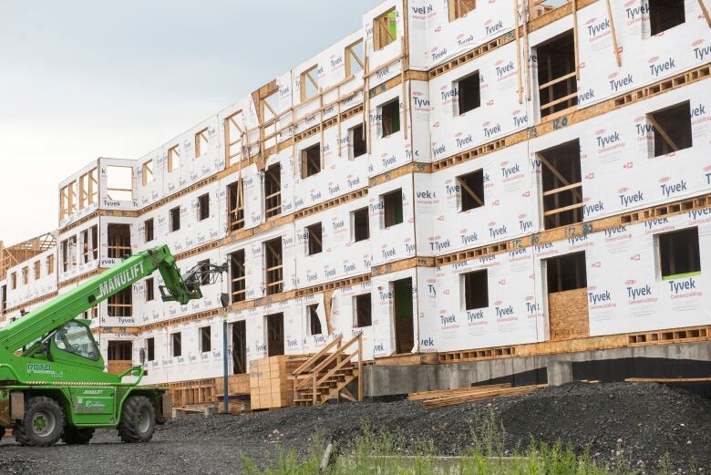 A green crane lift is pictured in front of an under construction apartment building. 