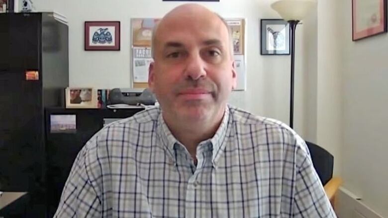 A man sitting in an office, wearing a plaid shirt.