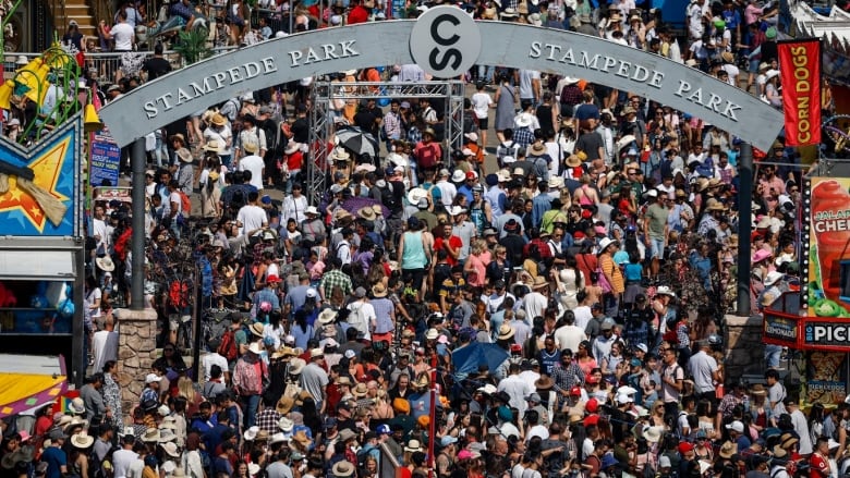 Hundreds of people, many wearing cowboy hats, enter the Calgary Stampede grounds under an arch bearing the words 