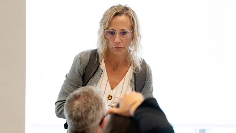 A woman with blond hair and glasses listens to a man with grey hair who is facing away from the camera.