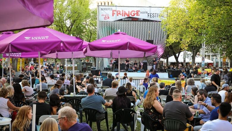 Dozens of people are pictured seated around tables in front of an outdoor stage.