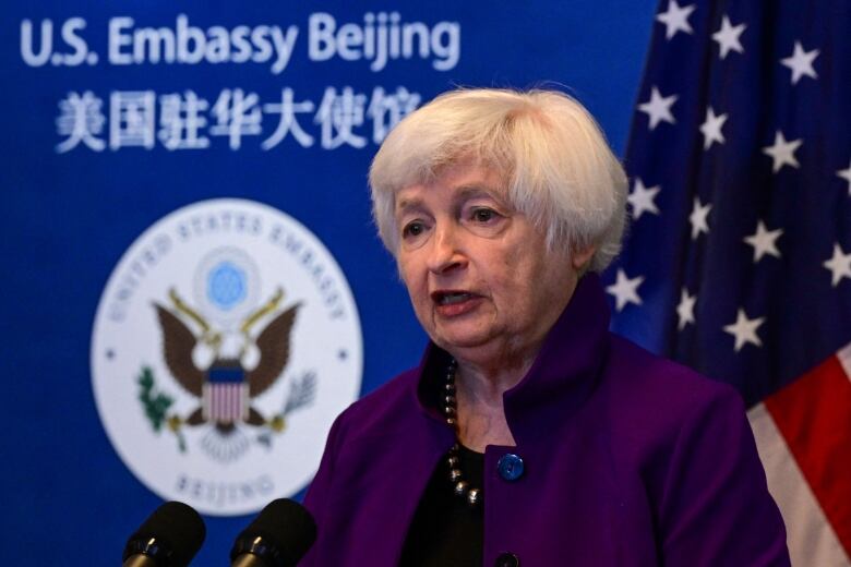 A woman in a blazer is shown speaking in front of an American flag and a backdrop that says, 'U.S. Embassy Beijing.'