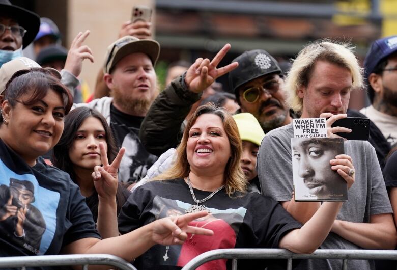 Fans make peace signs and hold up a photo at an outdoor event.