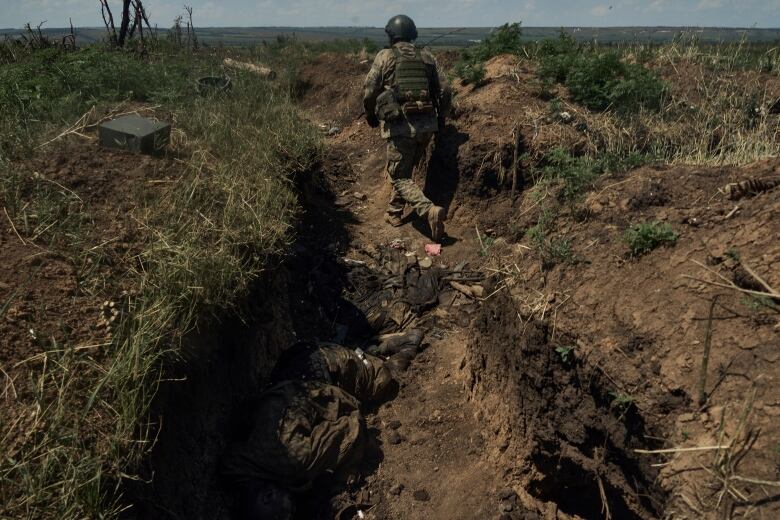 A Ukrainian soldier goes in a recently captured Russian trench with dead Russian soldiers, on the frontline near Bakhmut, Donetsk region, Ukraine, Tuesday, July 4 2023. Ukrainian forces are making steady progress along the northern and southern flanks of Bakhmut, in a semi-encirclement of the wrecked city that Russian forces have been occupying since May.