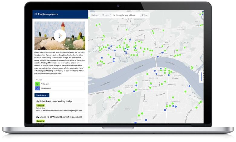 An interactive online map of the City of Fredericton is shown on the screen of a silver laptop, and the map is covered with bright green and blue dots.