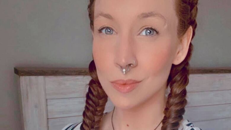 A woman with a nose ring and reddish hair in braids smiling.