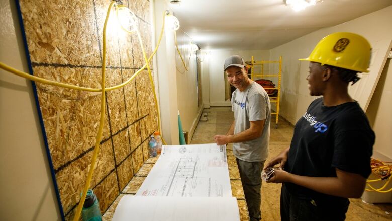 Tim Zubek, site supervisor with Building Up, and Dorine Khainza, an apprentice, are photographed in front of blueprints inside of a Toronto home under construction on July 6, 2023.