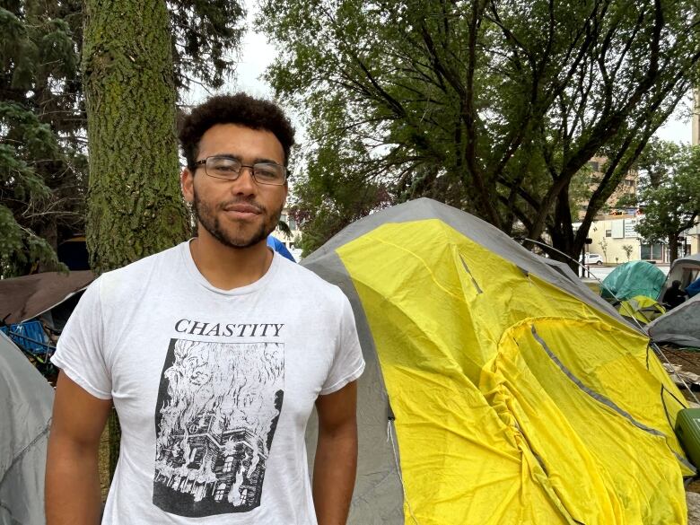 A man in a white shirt stands in front of a yellow tent. 