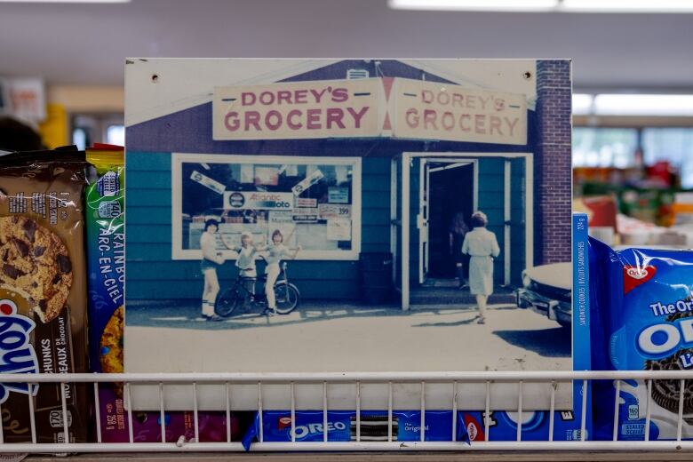 A photo of a picture that shows an old of a convenience store and young kids standing out front.