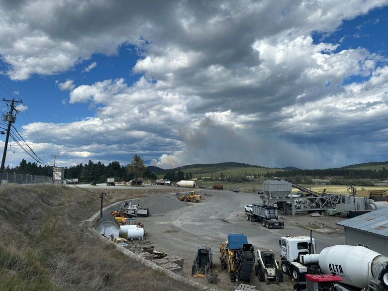 Smoke in the sky above a piece of land with many vehicles.