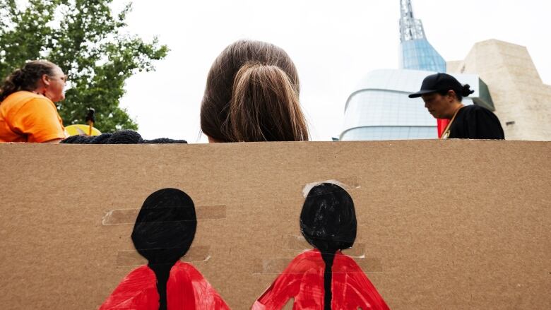 The back of a woman's head is seen in front of a sign with two women wearing red dresses.