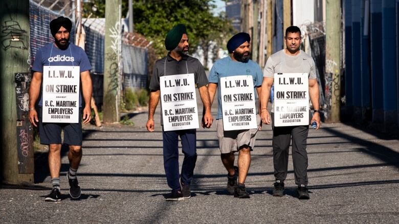 Four men walk with sandwich boards that read 'I.L.W.U. On Strike against B.C. Maritime Employers' Association'.