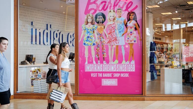 Women walk by a pink movie advertisement in a mall.