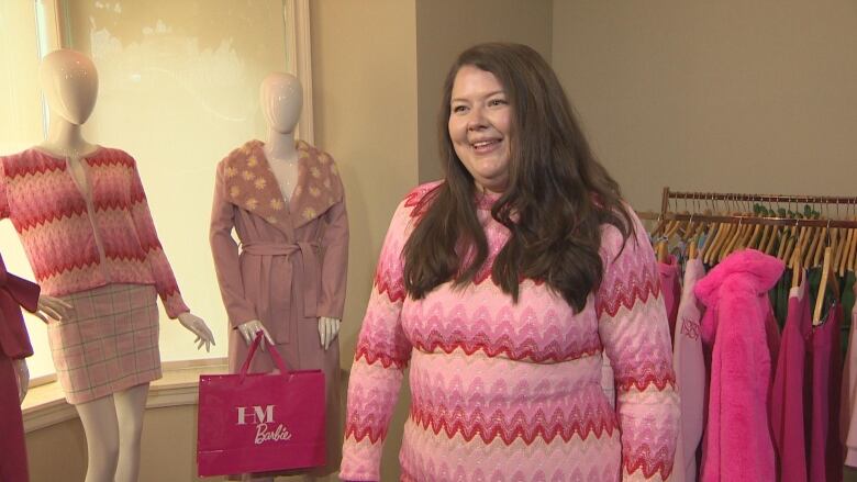 A woman in a bright prink dress stands in a dress shop.