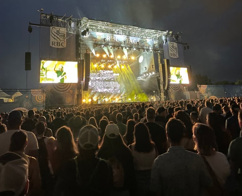 A crowd watches a rock band on stage at a festival at night.