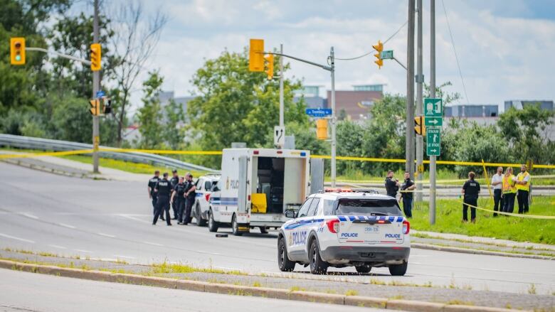 Police gather around police vehicles on a closed city road in summer.