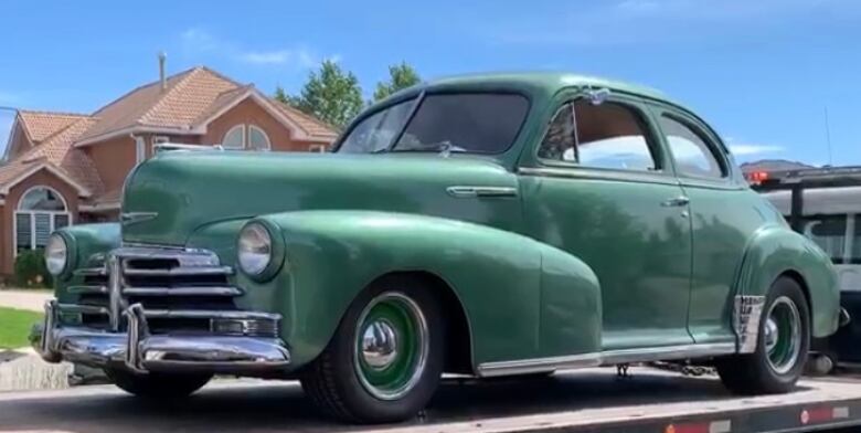 A green 1948 Chevy on the back of a trailer. The trailer is packed on a street.