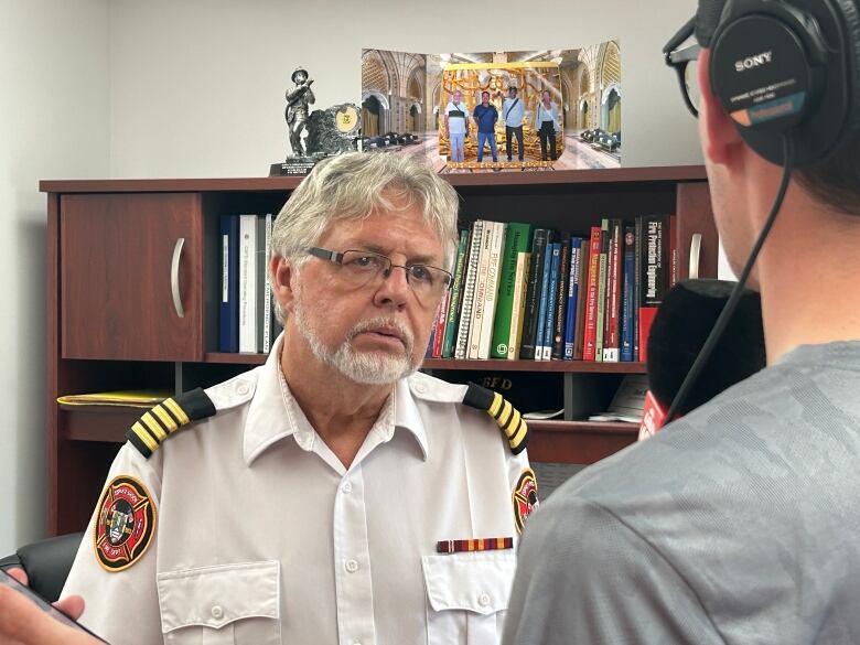 A man in a firefighters uniform speaks with a CBC reporter in his office.