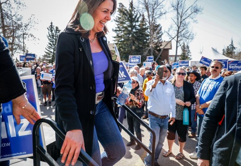 Politician descends stairs from stage as sign-waving supporters look on.