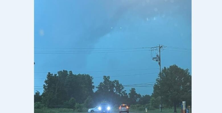 A photo through a car windshield of a dark funnel-looking cloud. 