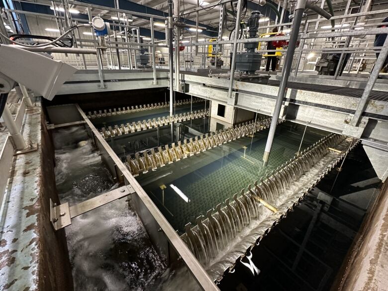 Water flows over a grate with various pipes, catwalks and other systems in the background.