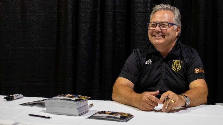 A man sits a table smiling wearing a Las Vegas Golden Knights polo.