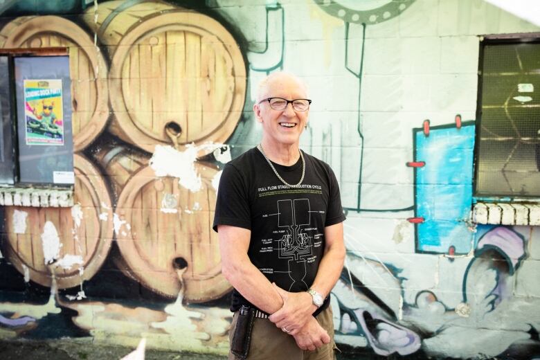 A man poses in front of a mural that depicts beer pouring out of barrels.