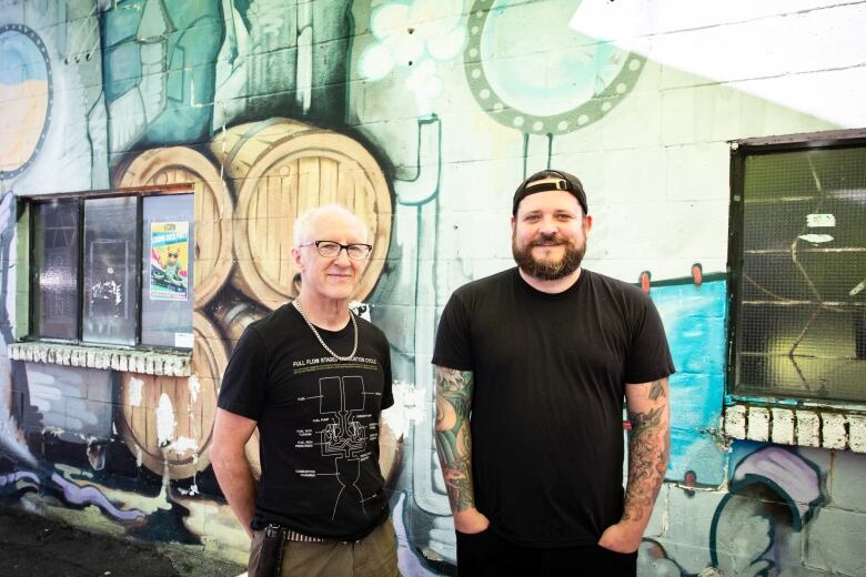 Two men in front of a mural depicting beer barrel.