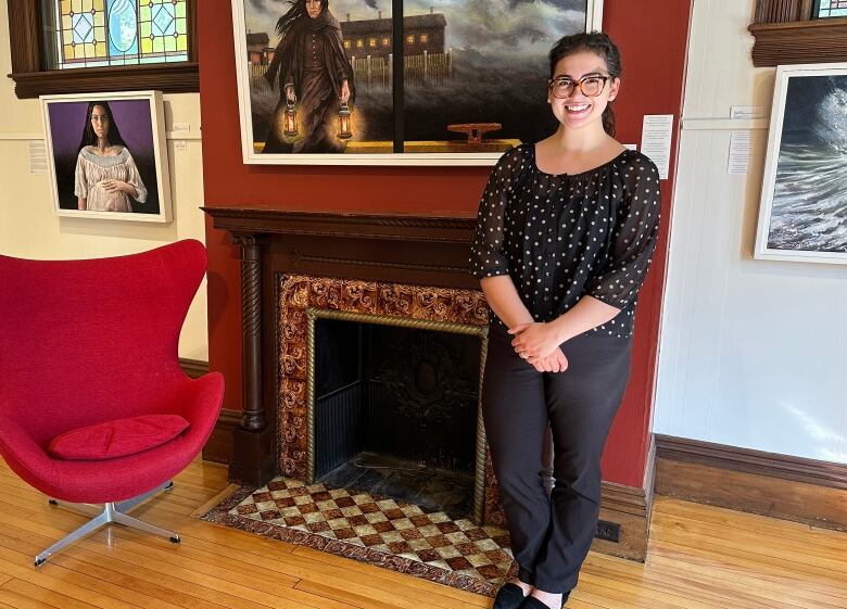 A woman standing next to a fireplace surrounded by art work on the walls.