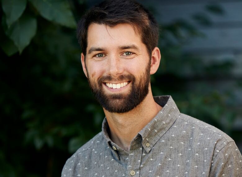 A man posing and smiling in front of a background of leaves