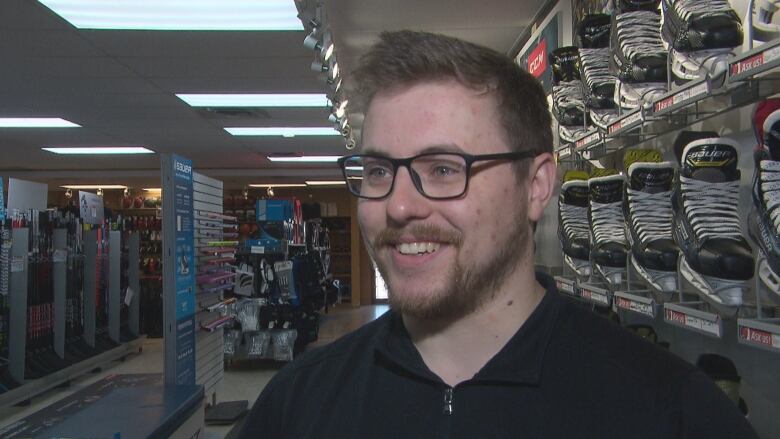 A man smiling in front of a wall of hockey skates