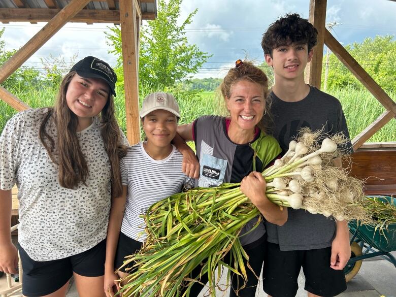 Three students and a woman holding garlic smile at the camera