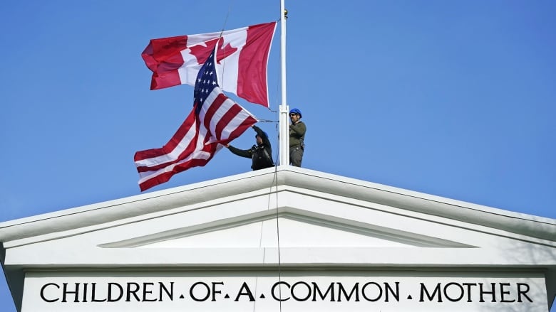 Canadian and American flags fly atop a monument.