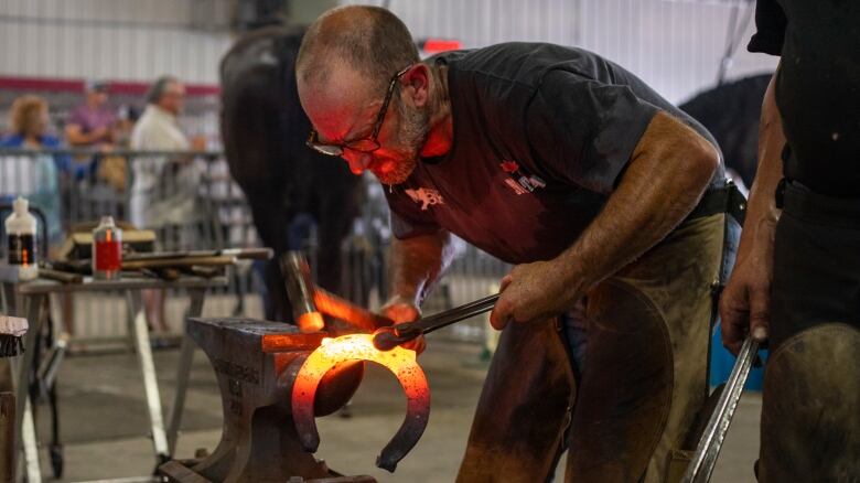 A blacksmith hammers a hot horseshoe on an anvil.