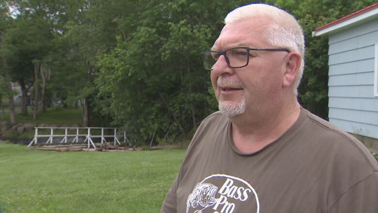 A man in a taupe t-shirt speaks to the camera.