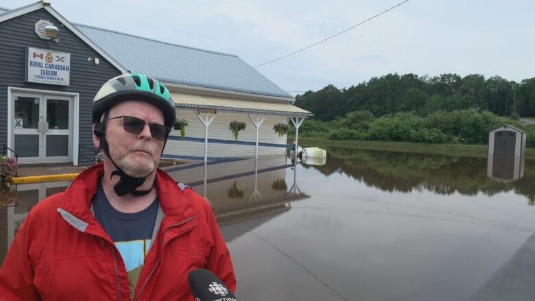 A man in a bike helmet and red jacket stand in front of a parking lot filled with ankle high water.