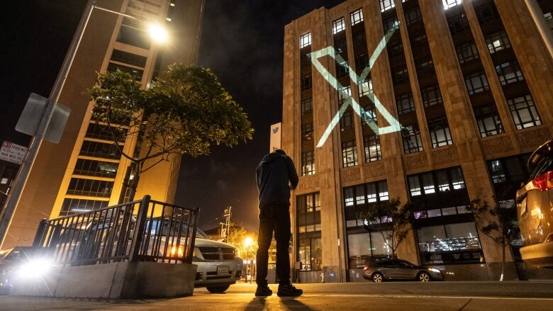 A large X is projected onto a building at night.