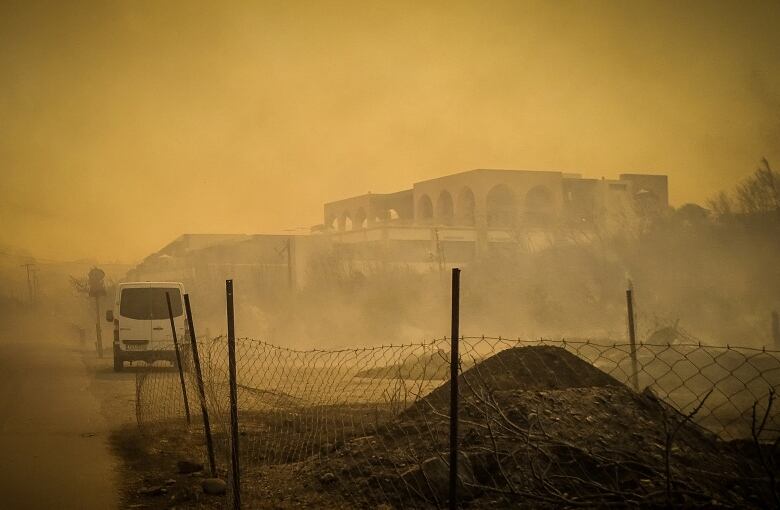 The smoke of a wildfire near a burnt-out hotel.