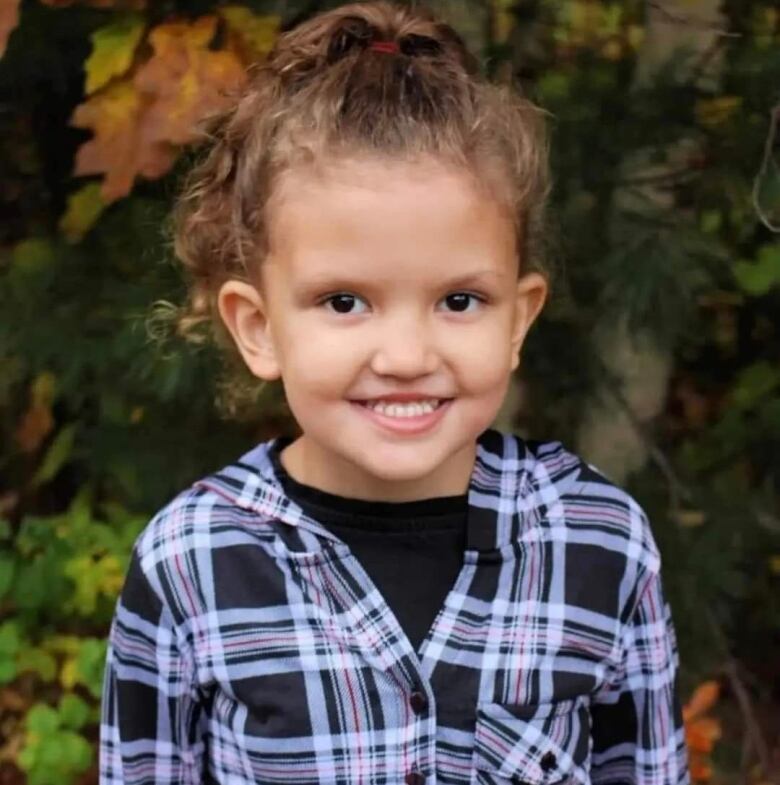 Girl wearing blue, pink and purple plaid shirt is smiling.