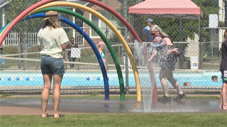 Mother holding toddler in play fountain.