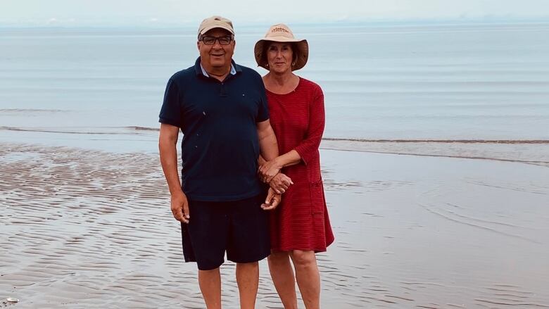 A man and woman with their arms entwined at the water's edge on a beach.