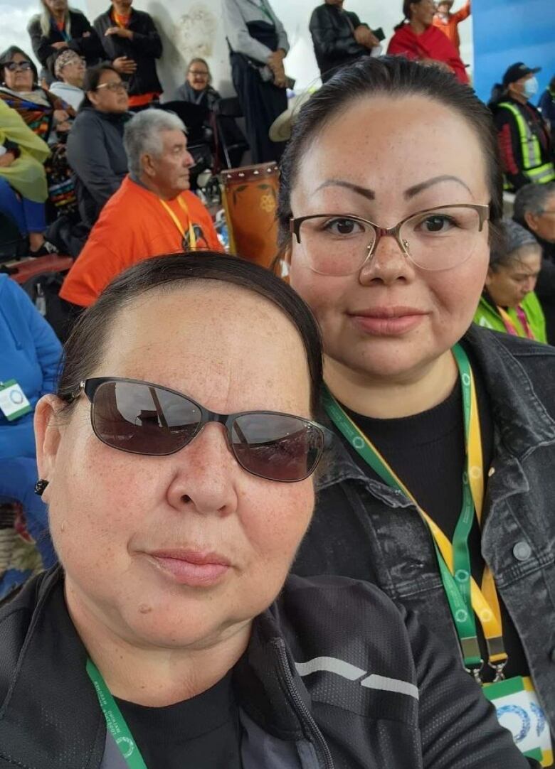 Two women pose for a selfie in the audience of a papal ceremony.