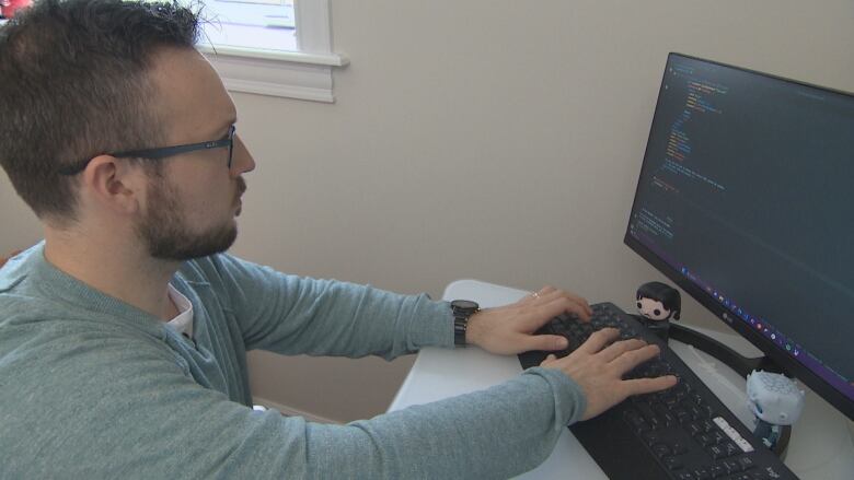 A man sits in front of a computer, typing code.