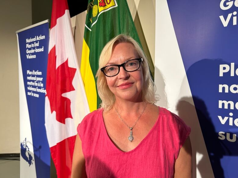 A woman in pink dress stands in front of Canada's flag.